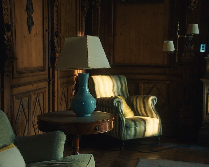 Well-lit vintage living room interior with striped armchair, blue vase, side table and wood paneling, creating a cozy, traditional aesthetic.