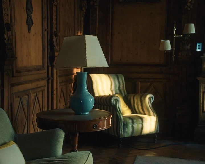 Well-lit vintage living room interior with striped armchair, blue vase, side table and wood paneling, creating a cozy, traditional aesthetic.