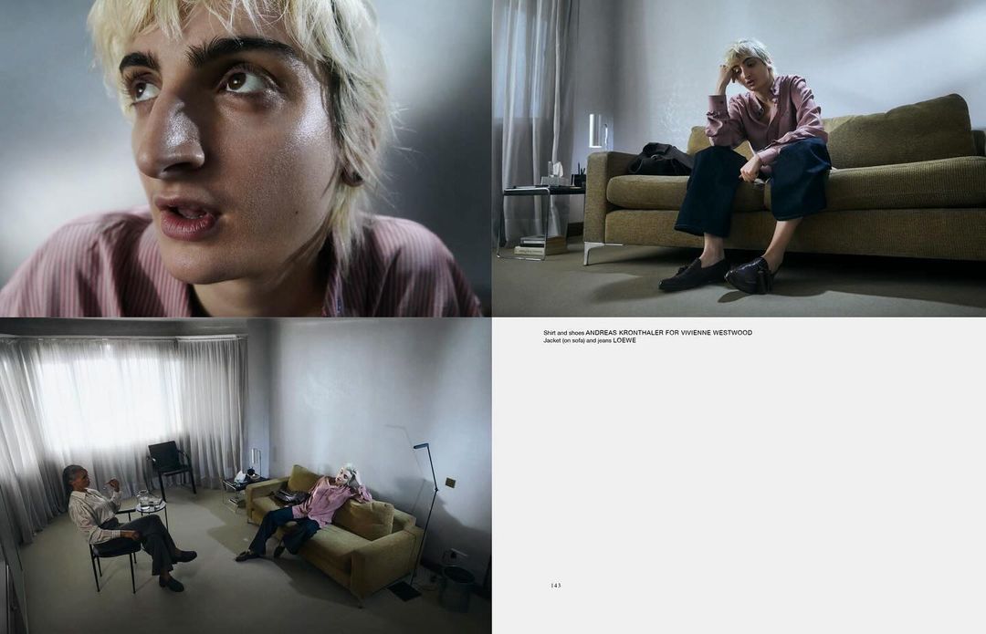 Man with blonde hair sits thoughtfully on a green couch in a minimalist room, in a fashion editorial with subdued lighting and a introspective mood.