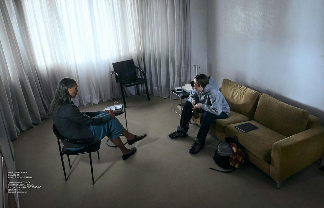 Two people seated in a modern living room, one in a chair facing another person sitting on a mustard yellow sofa