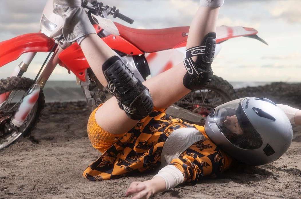 Outdoor shot of a person wearing protective gear and a helmet lying on the ground next to a red and white dirt bike.