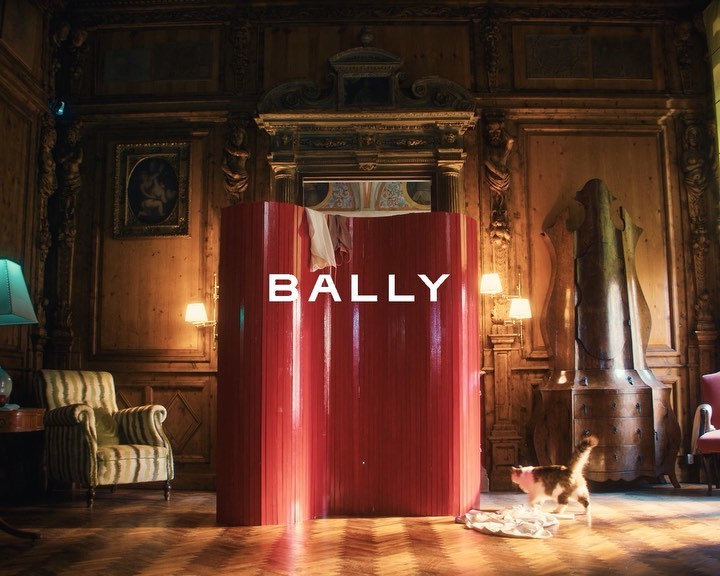 Ornate interior with 'BALLY' text on a modern red structure, featuring a cat, lamp, striped chair, and wooden parquet flooring.