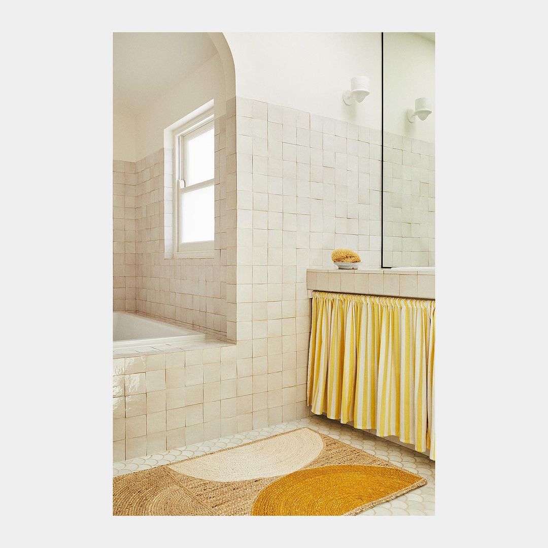 Bathroom interior with tiled walls, bathtub, decorative rug, and vanity with striped curtain, creating a clean and modern aesthetic.
