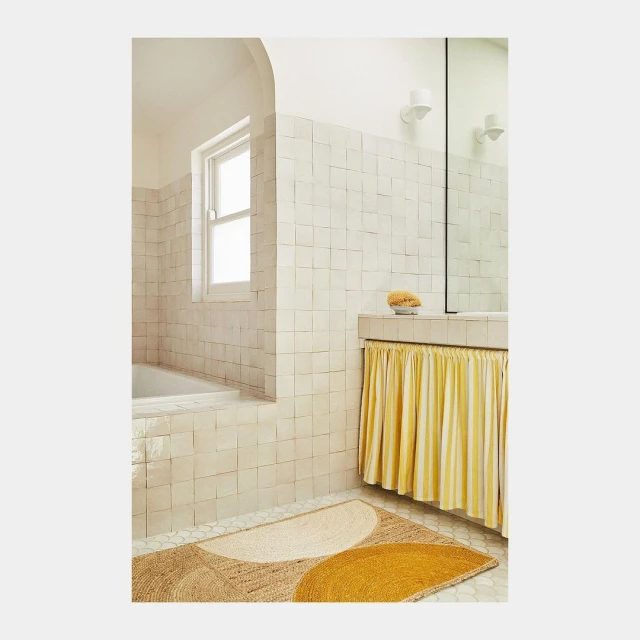 Bathroom interior with tiled walls, bathtub, decorative rug, and vanity with striped curtain, creating a clean and modern aesthetic.