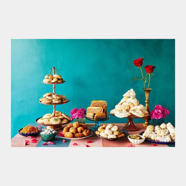 Table filled with a variety of Middle Eastern and Persian sweets, cookies, and pastries, set against a vibrant teal backdrop.