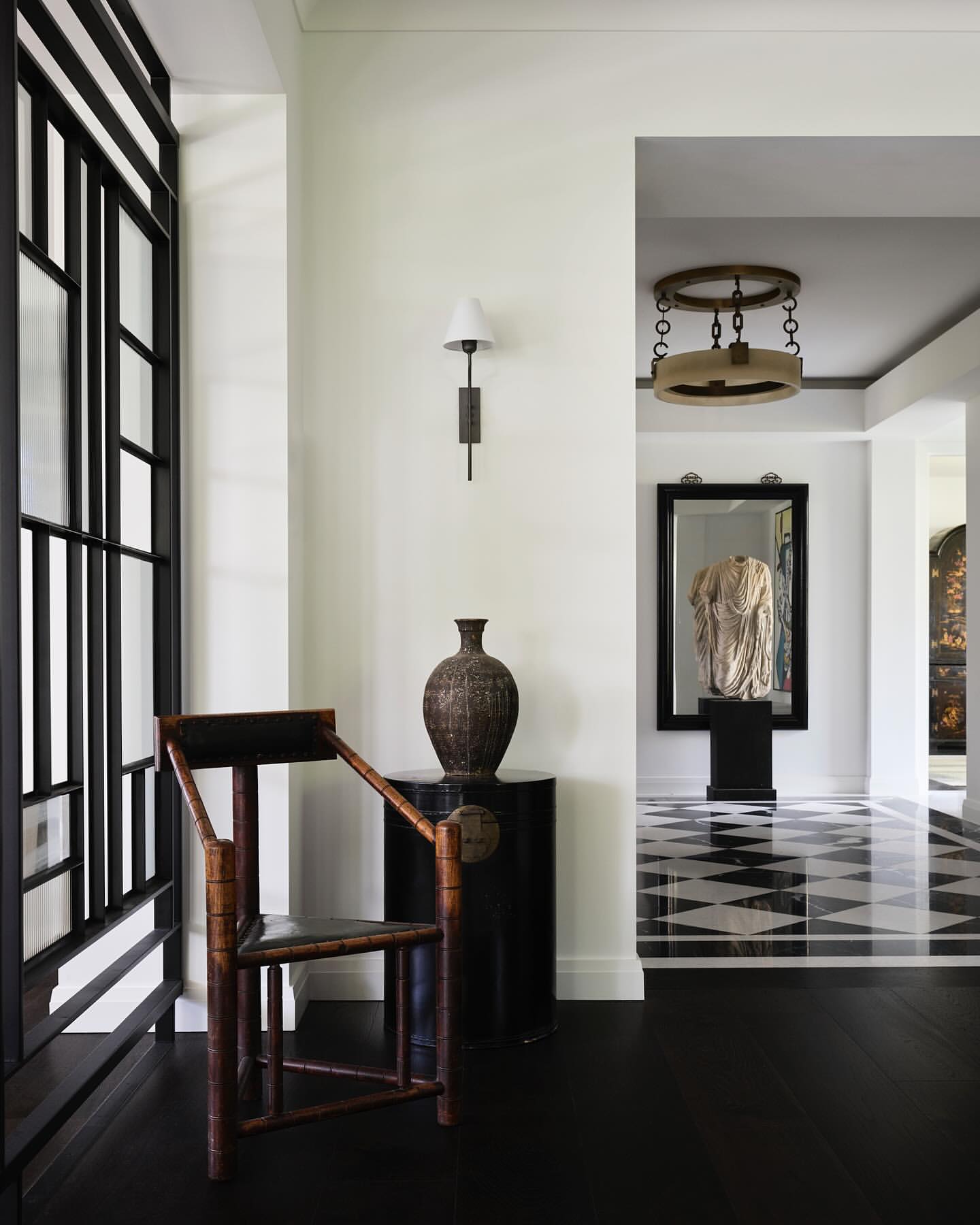 Interior view of a hallway featuring a wooden chair, decorative vase on a black table, and a geometric black and white floor design.