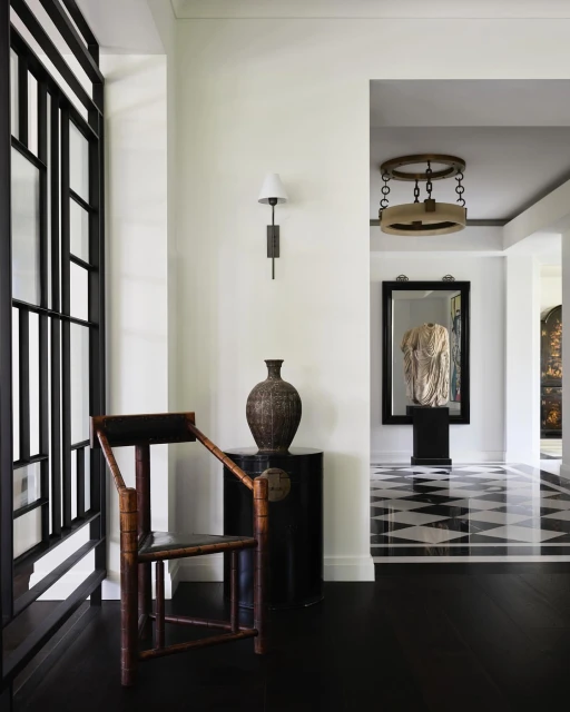 Interior view of a hallway featuring a wooden chair, decorative vase on a black table, and a geometric black and white floor design.