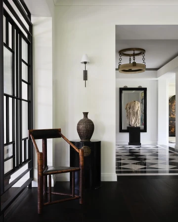 Interior view of a hallway featuring a wooden chair, decorative vase on a black table, and a geometric black and white floor design.
