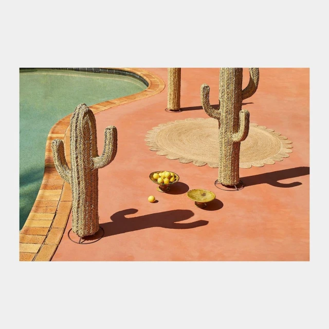Outdoor poolside patio with decorative woven cactus sculptures, lemon-filled bowls, and a round mat, creating a serene, artistic space.