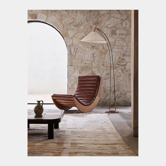 Interior shot of a modern living room featuring a brown leather lounge chair, a floor lamp, a coffee table with decor, and a stone wall.