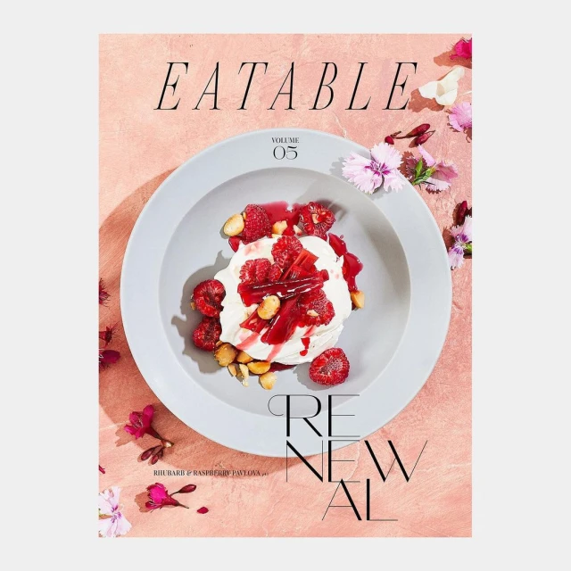 Overhead shot of a food magazine cover featuring a dessert topped with raspberries, styled with delicate flowers on a textured surface.