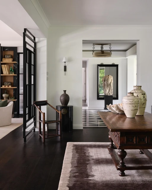Interior of a home featuring a wood table with decorative vases, a dark wood floor, and white walls, with dark accent elements.