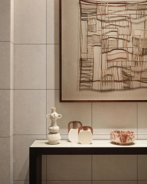 Still life featuring three vases and a bowl on a black and white console table against a neutral tiled wall with framed art.