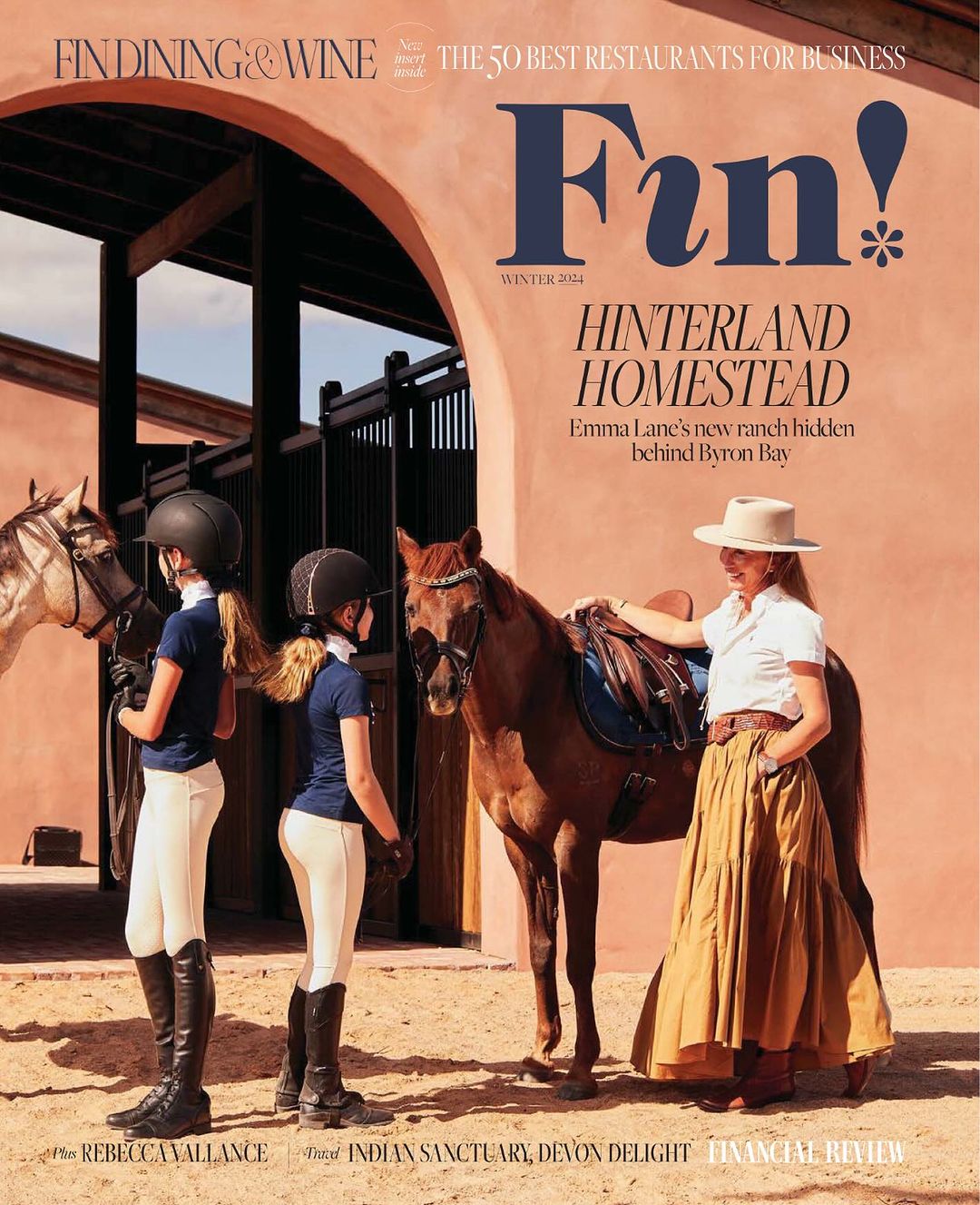 Magazine cover featuring two girls with horses and an adult female in a skirt, standing outside a stable on a sunny day.