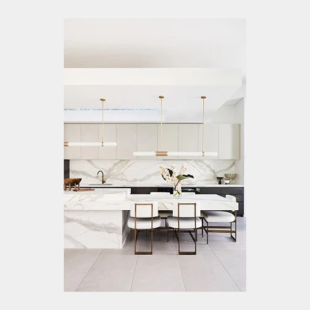 Modern kitchen and dining area featuring marble countertops, white cabinetry, gold accents, pendant lights, and seating for six.