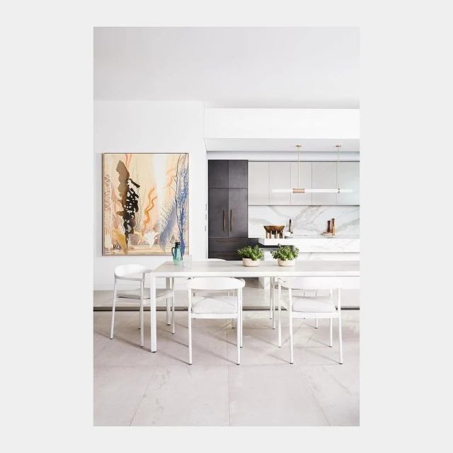 Interior dining area with white table and chairs, accented by an abstract painting, in a modern home with a kitchen background.