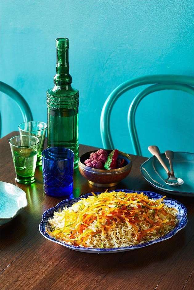 Overhead shot of an ornate table holding a bottle, glasses, dish of rice and carrots, and a small bowl of purple vegetables.