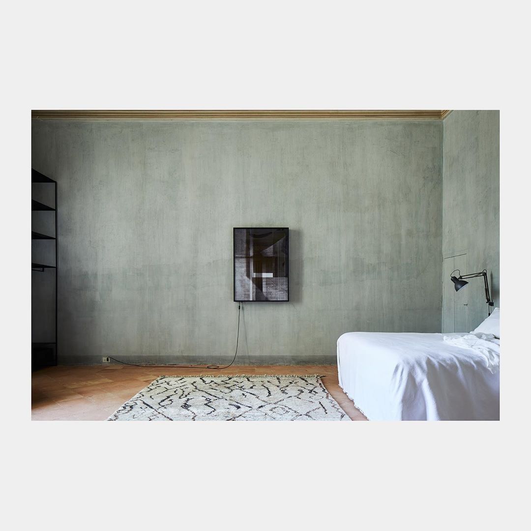 Minimalist bedroom with light green walls, black framed art, white bed, patterned rug, and a black floor lamp creating a simple aesthetic.