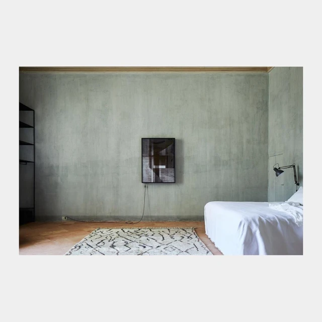Minimalist bedroom with light green walls, black framed art, white bed, patterned rug, and a black floor lamp creating a simple aesthetic.