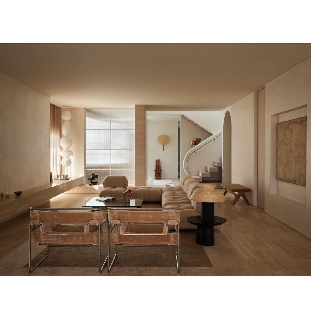 Living room interior featuring modern furniture, including armchairs, a sectional sofa, and a glass coffee table on a neutral rug.