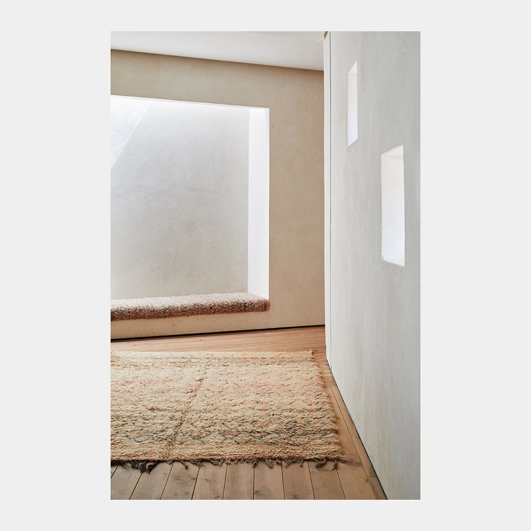 Minimalist interior featuring a rug on wood flooring, a cushioned nook, and natural light creating a serene and inviting space.