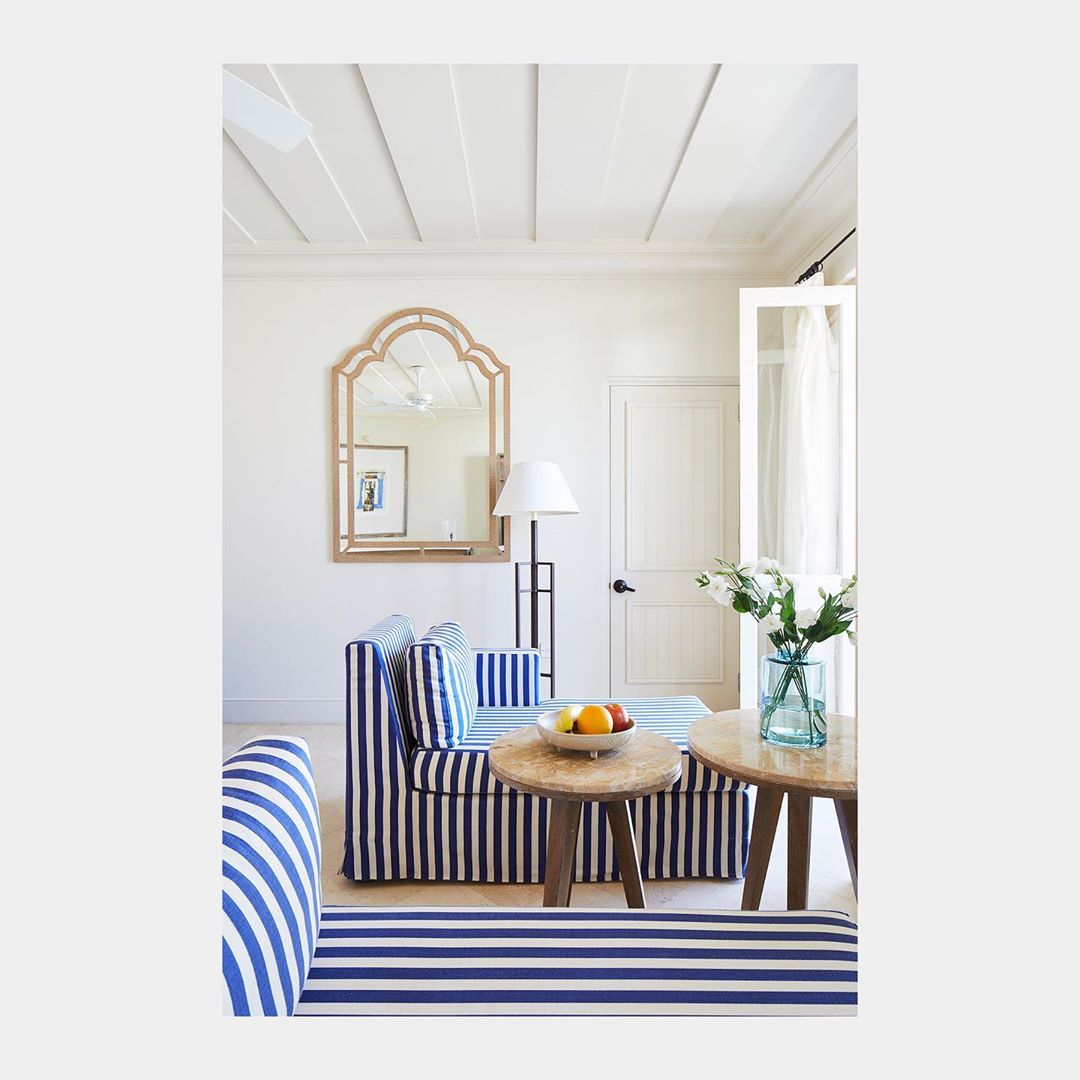 Living room interior with blue and white striped sofa, wooden side tables, vase of white flowers, mirror, lamp, and white walls and ceiling.