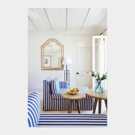 Blue and white striped sofa in a bright living room with wooden coffee tables and a framed mirror on the white wall.