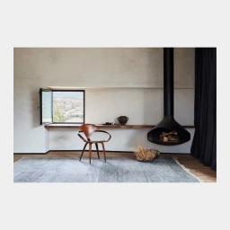 Interior photography featuring a wooden chair and a black hanging fireplace in a minimal room by Alicia Taylor