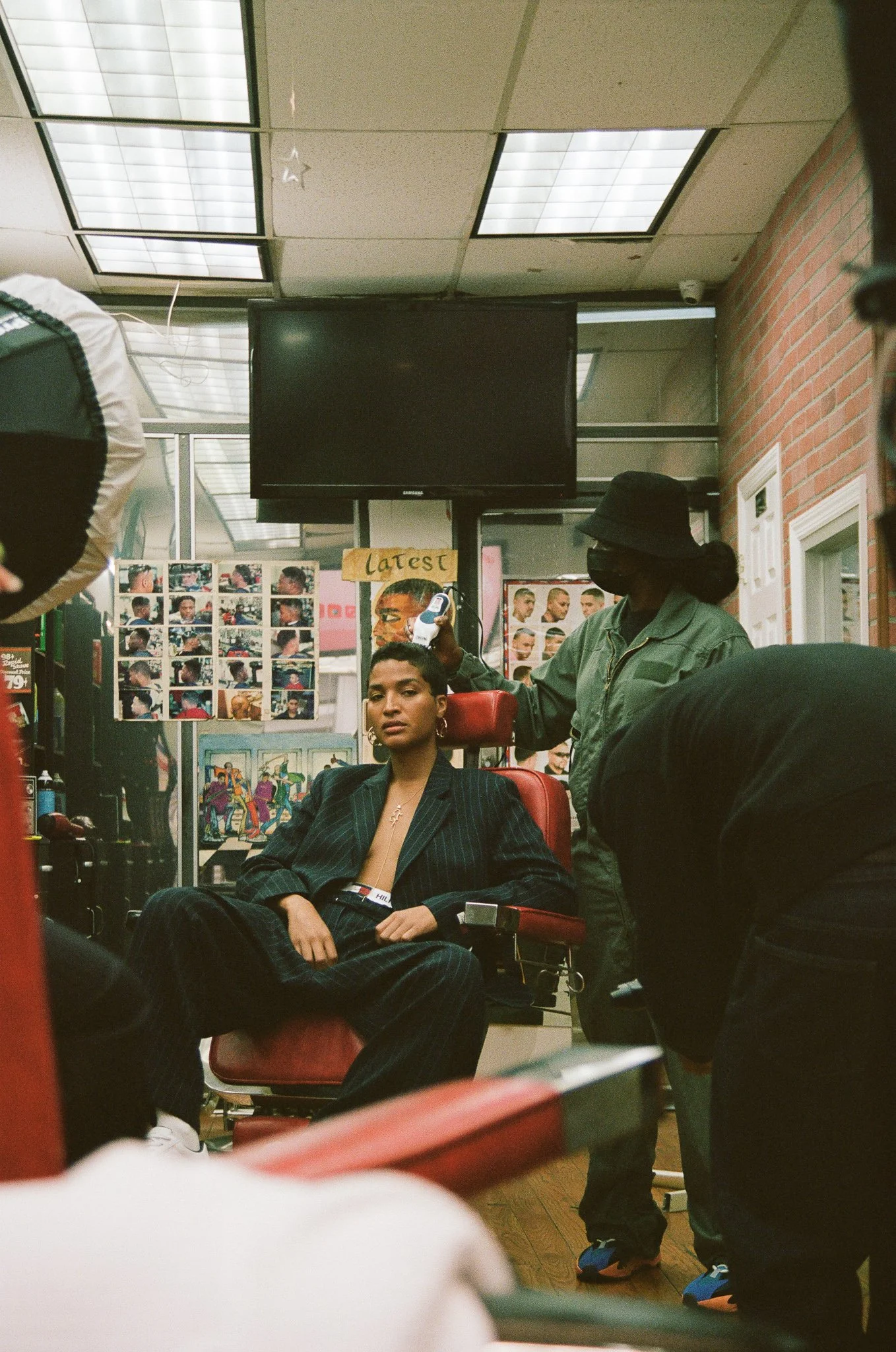 Barbershop scene featuring a model seated in a barber chair with a barber cutting his hair, surrounded by barber shop equipment.