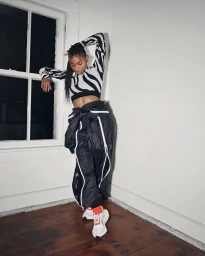 Model wearing a zebra-print cropped top and oversized black track pants with white piping posing on a wooden floor.