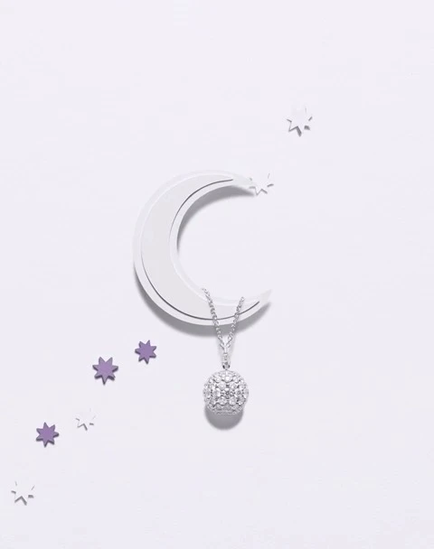 Elegant pendant necklace with a sparkling round diamond and set on a white surface with moon and star accents for luxury jewelry advertising.
