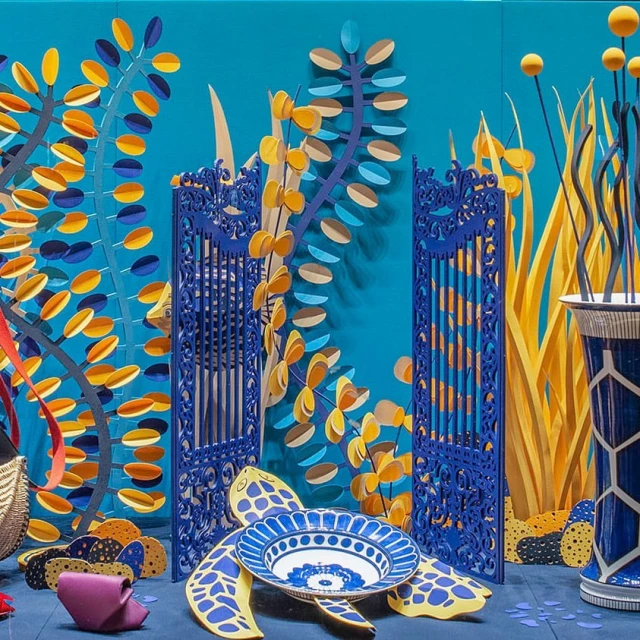 Colorful display with blue gates, paper plants in yellow and blue, and a ceramic turtle bowl on a blue surface creates an underwater scene.