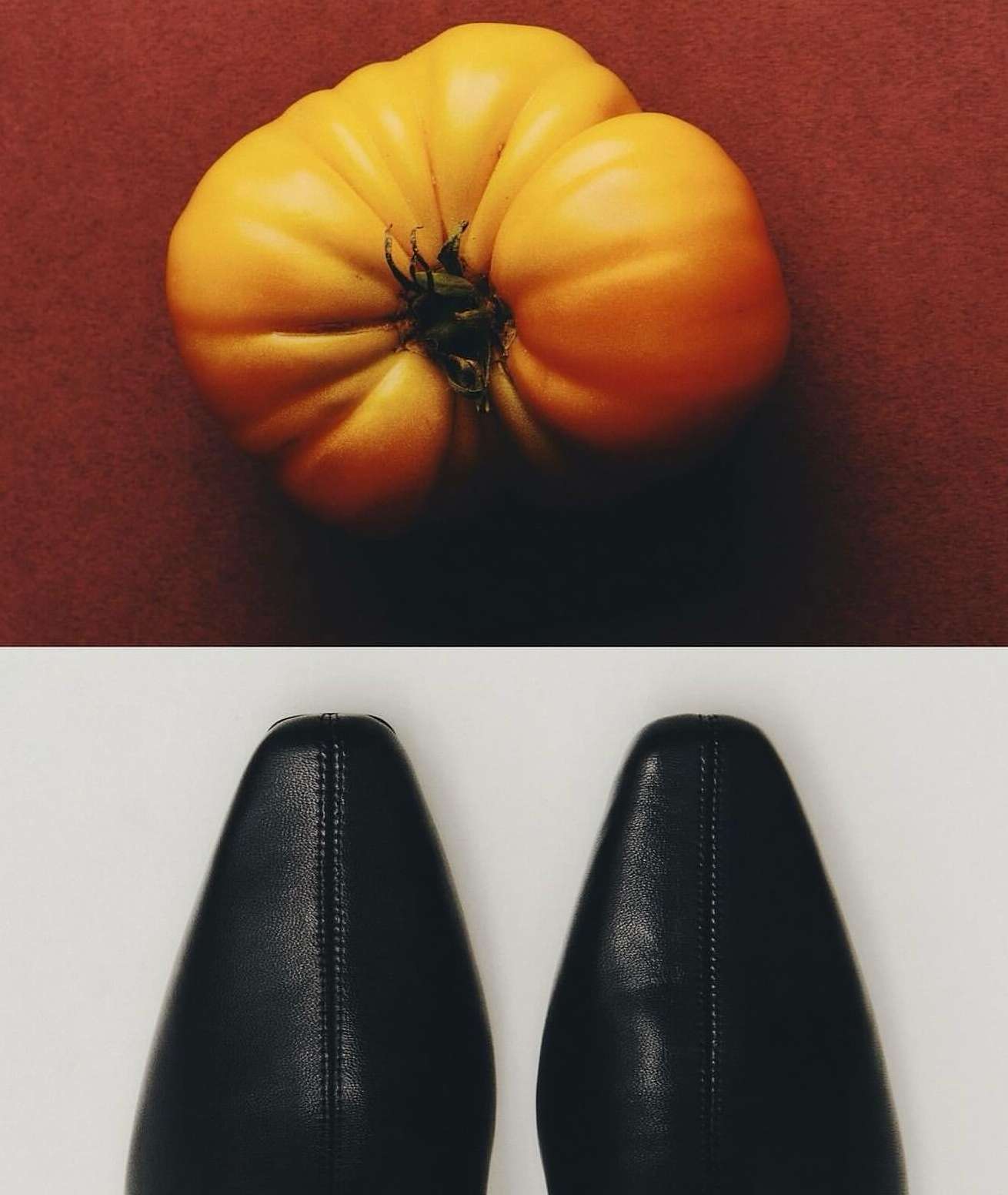 Still life of a yellow heirloom tomato on a red surface with two black leather dress shoes on a white surface below it.