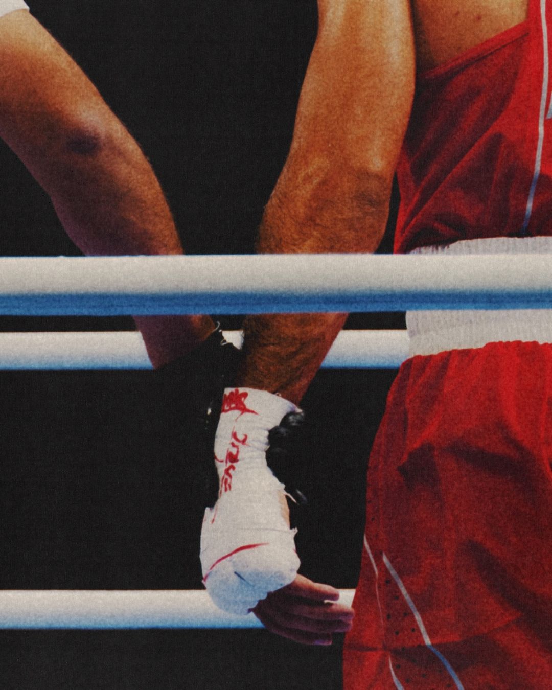 Close-up view of boxers in the ring, one with wrapped hands. Focus on the arms and hands in the boxing ring, vibrant red and blue.