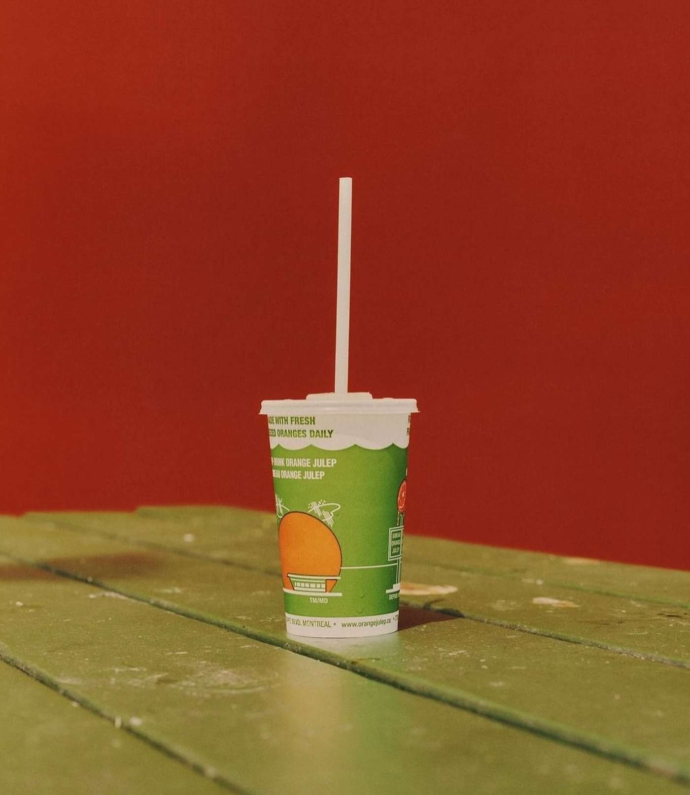 Green juice cup with a white straw on a green wooden table against a red background creates a bold, eye-catching still life.