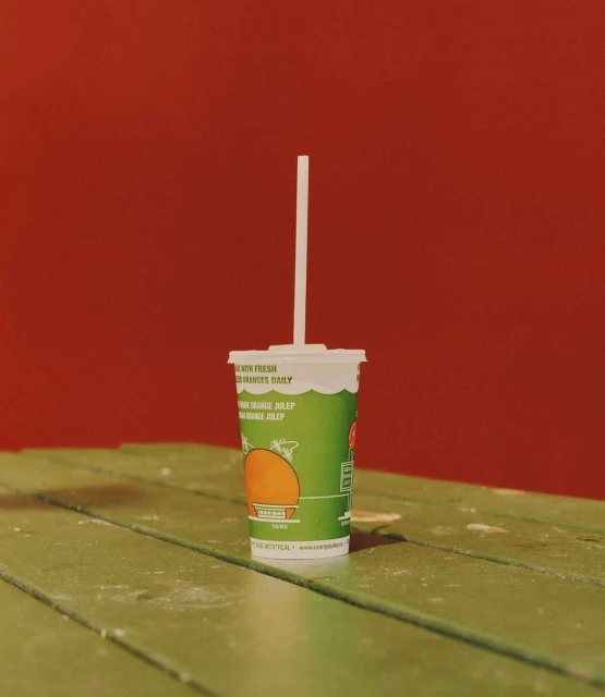Green juice cup with a white straw on a green wooden table against a red background creates a bold, eye-catching still life.