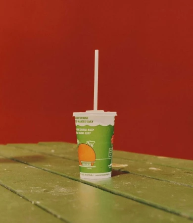 Green juice cup with a white straw on a green wooden table against a red background creates a bold, eye-catching still life.
