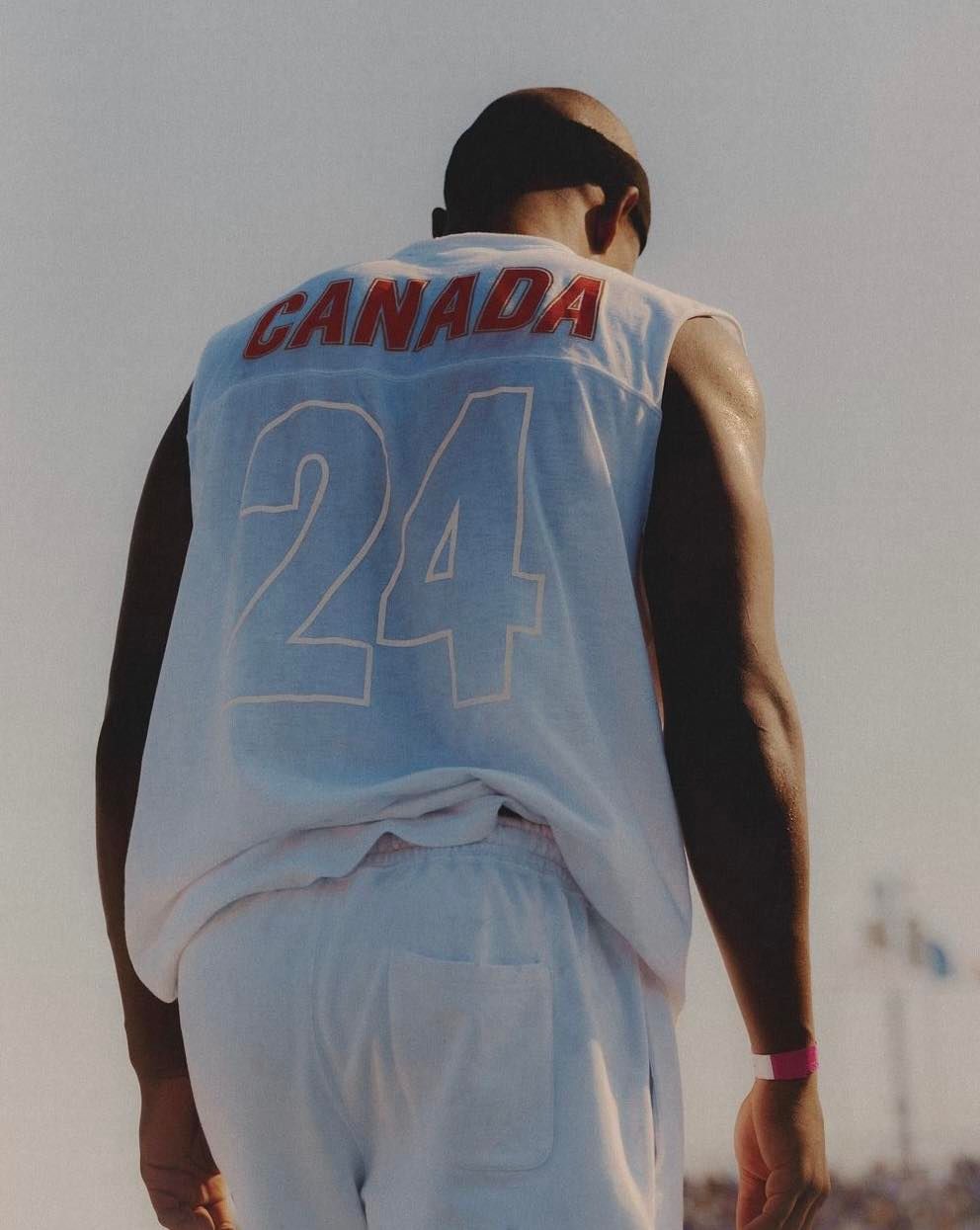 Close-up shot from behind of an adult male athlete with a shaved head wearing a Canada jersey and white athletic shorts.