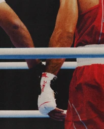 Close-up of a boxer in red shorts and taped hands touching gloves across ring ropes in a ring shot by Aliocha Boi