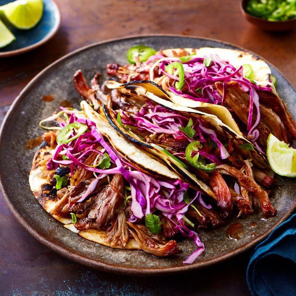 Overhead shot of a plate with three vibrant tacos filled with shredded meat, red cabbage, jalapenos, cilantro, and a lime wedge.