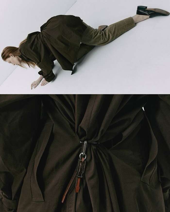 Fashion shot of a woman in a long brown coat and pants, lying on a white surface with part of the coat filling the frame.