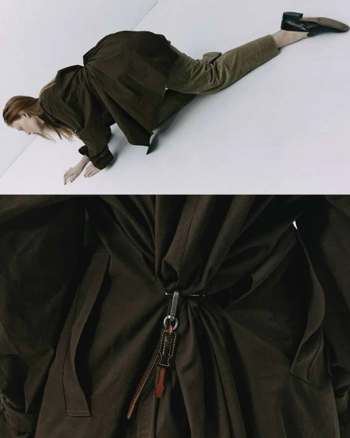 Fashion shot of a woman in a long brown coat and pants, lying on a white surface with part of the coat filling the frame.