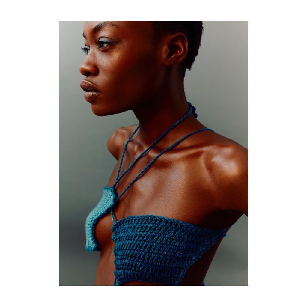 Portrait of a Black woman wearing a blue crocheted top, looking off to the side in a close-up studio shot with neutral background.