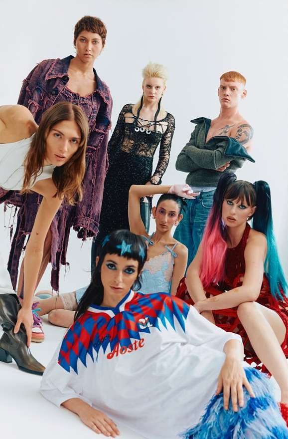 Group of seven diverse fashion models in a studio setting, showcasing a variety of textured and colorful clothing, and unique hairstyles.