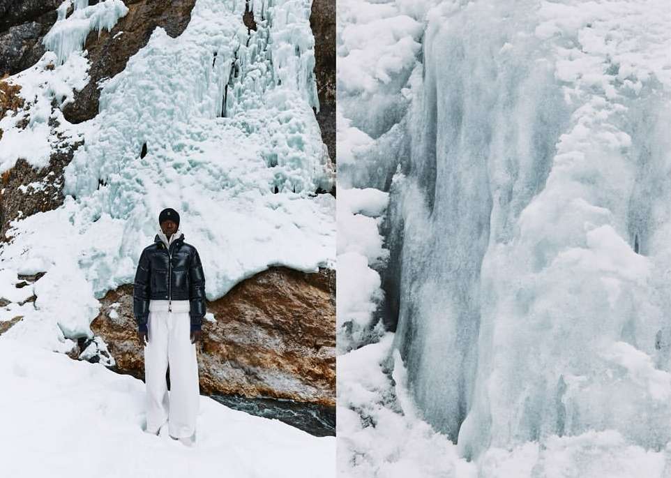 Fashionable adult stands out in a winter landscape wearing a black jacket and white pants near an icy waterfall.