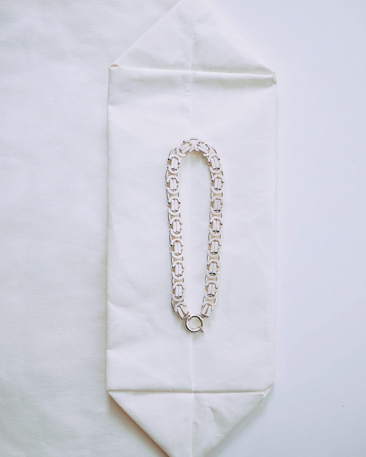 Overhead shot of a silver-toned metal link chain necklace with a toggle clasp on a folded white paper background.