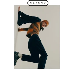 Model in orange beanie and striped sweater leaning against a white studio wall photographed by Alizee Omaly
