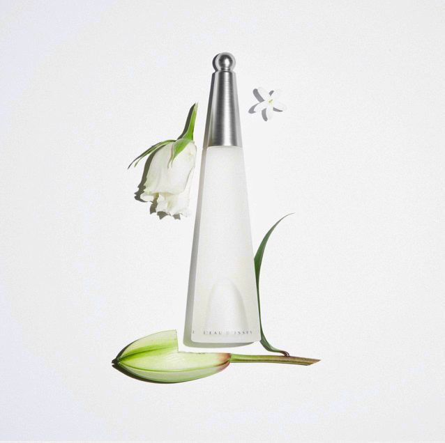 Issey Miyake L'Eau d'Issey perfume bottle with white rose, lily bud, and jasmine flower on a solid white background in a beauty shot.