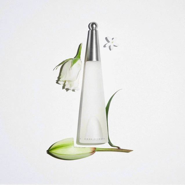 Issey Miyake L'Eau d'Issey perfume bottle with white rose, lily bud, and jasmine flower on a solid white background in a beauty shot.