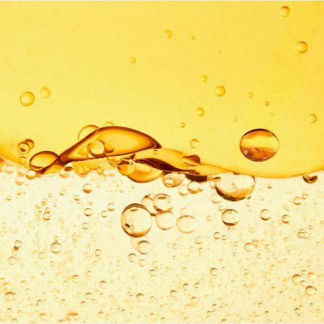 Close-up of small yellow liquid bubbles suspended in clear liquid, creating an abstract, effervescent, and textured appearance.